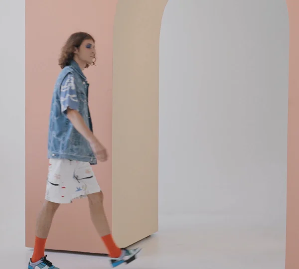 A frame of a person in a denim shirt and shorts walking in a studio, from the recorded demonstration clip.